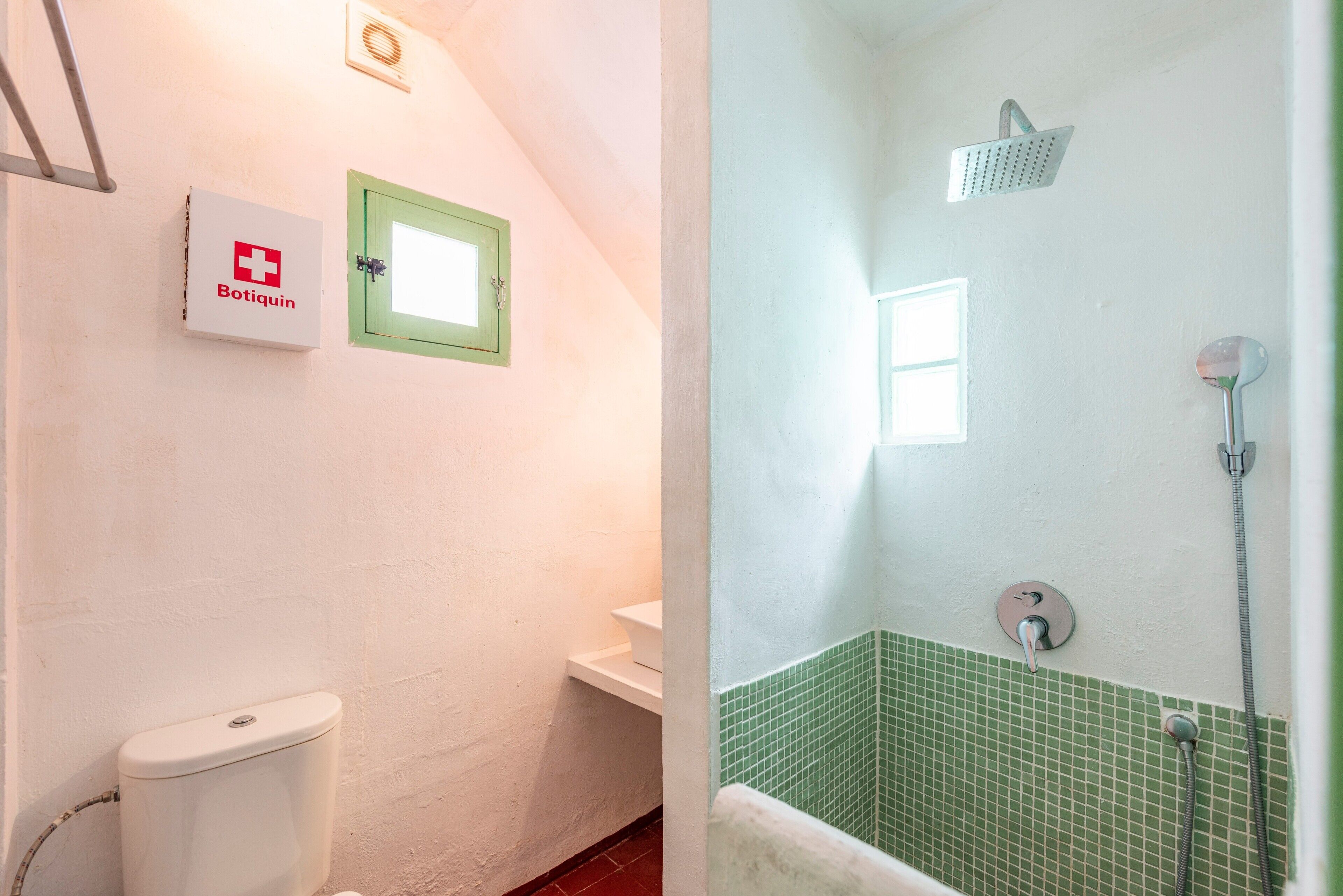 Une salle de bain comprenant des toilettes, un lavabo, une douche avec un mur recouvert de carreaux verts et un panneau de commande fixé au mur.