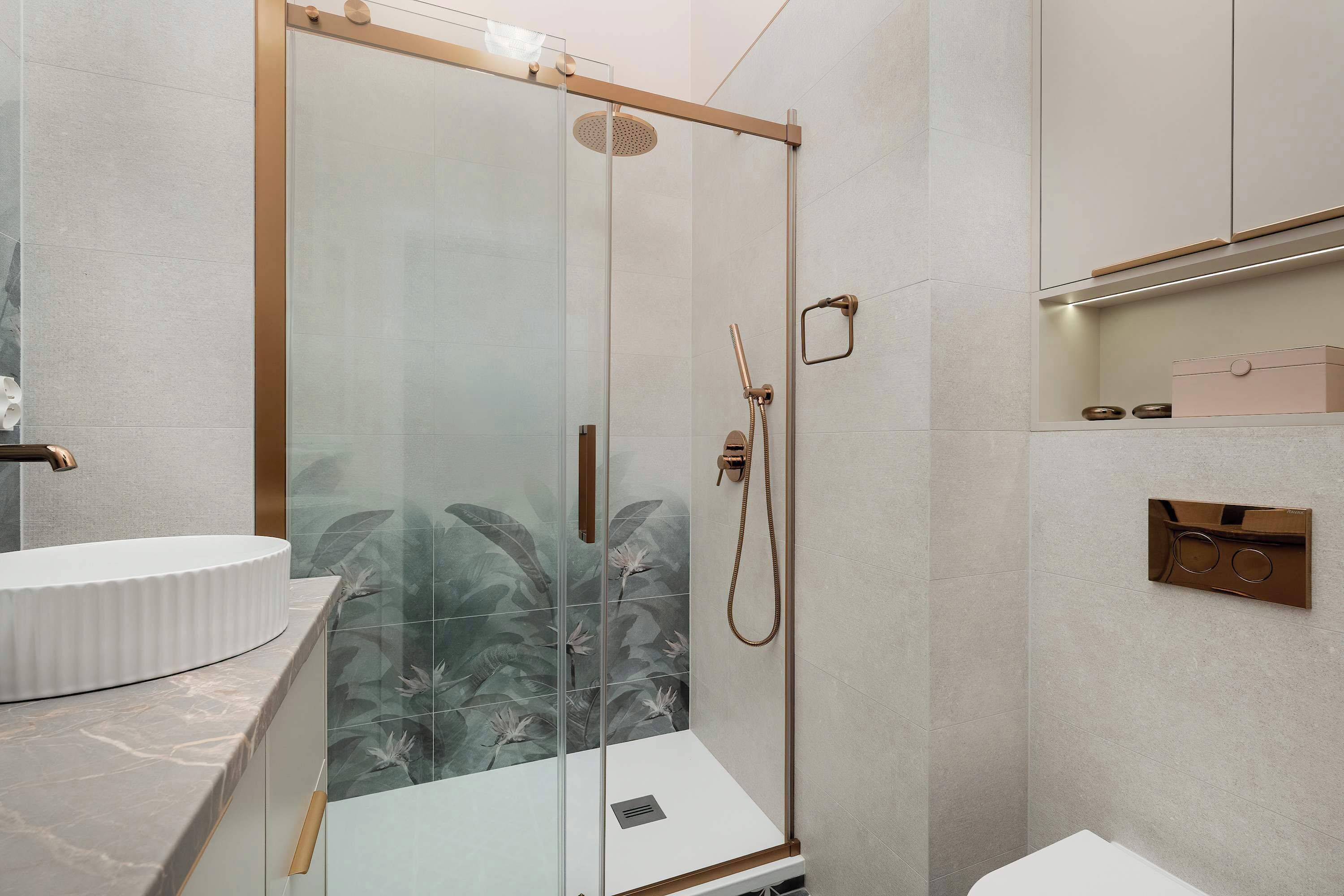 Une salle de bain moderne avec une douche à l’italienne en verre, un lavabo blanc et un plan de toilette en marbre.