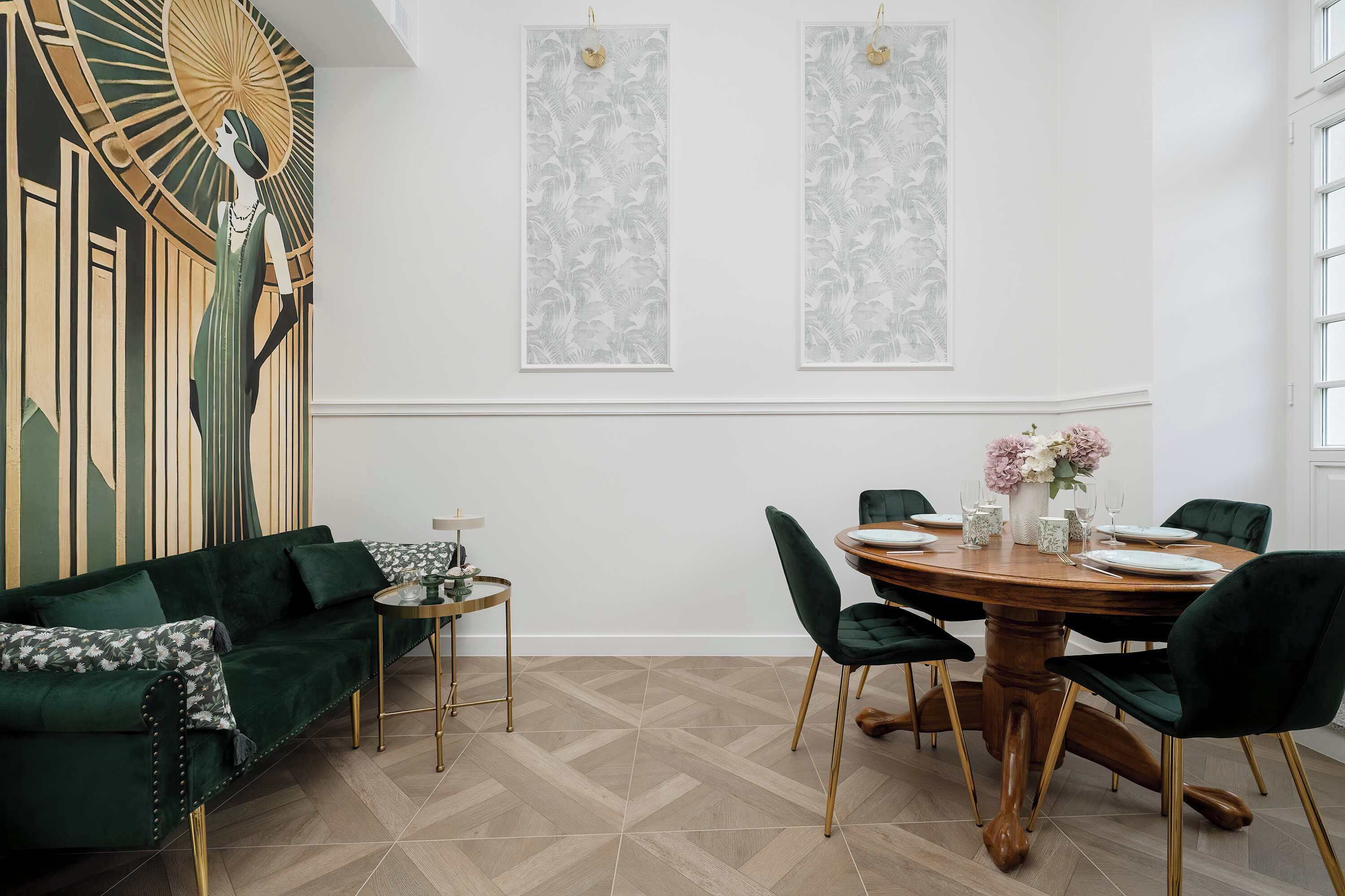 Ein Essbereich mit einem runden Holztisch, grünen Polsterstühlen und einer Blumenarrangement.