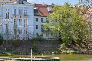 Vista al río de un edificio de varios pisos con balcones, un río en primer plano y árboles al fondo.