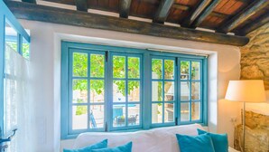 Un dormitorio con un ventanal grande, una cama con sábanas blancas y una lámpara a un lado.