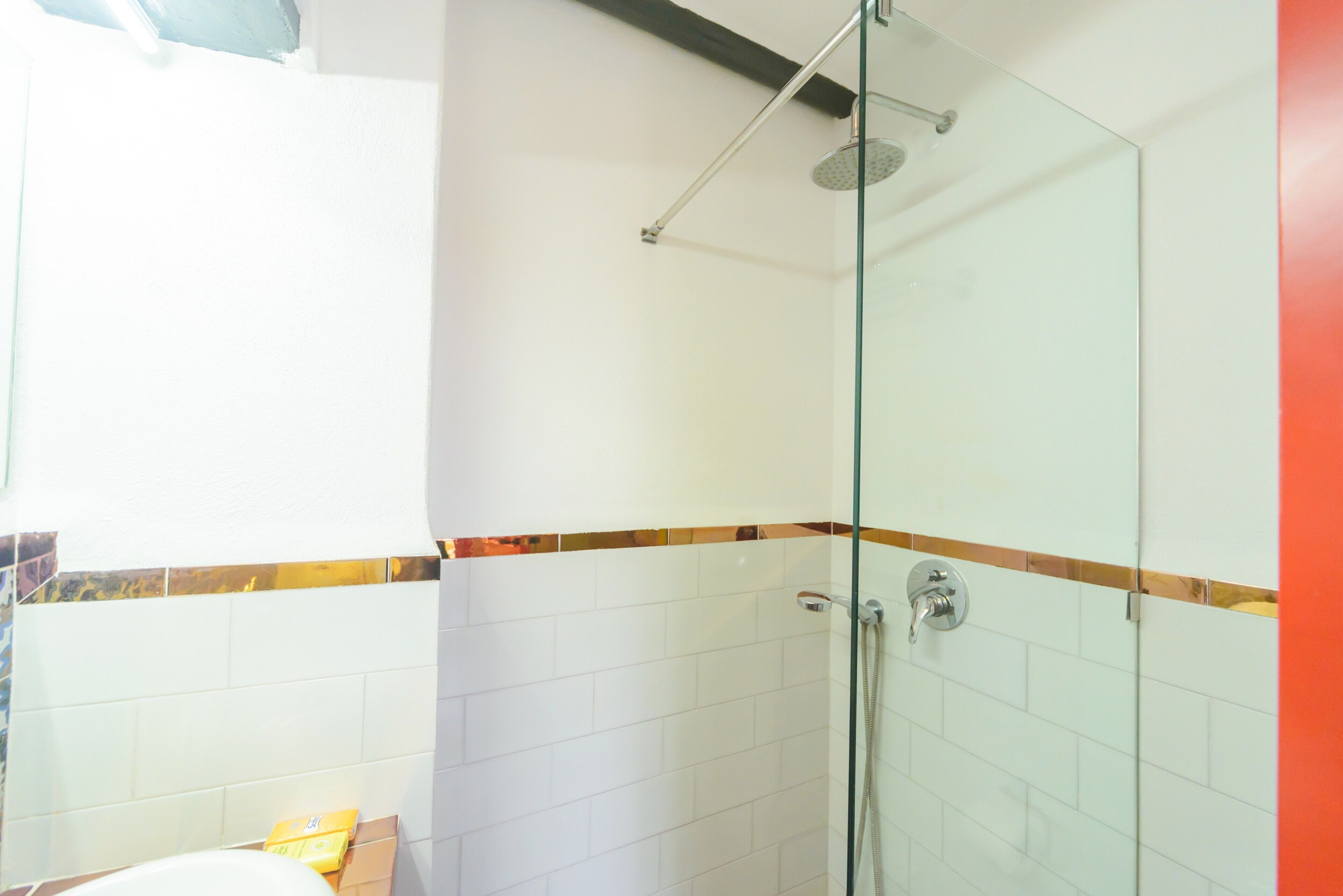 Een douche met glazen wanden, een handdouche, witte betegelde muren en een handdoekhouder.