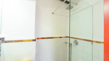 Een douche met glazen wanden, een handdouche, witte betegelde muren en een handdoekhouder.