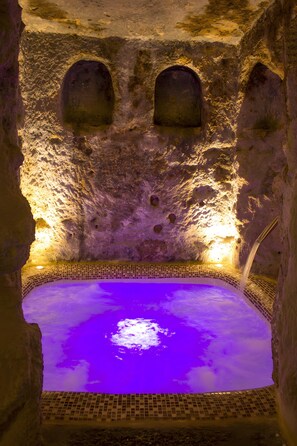 Un spa con piscina iluminada en morado, paredes de piedra y suelo de baldosas.