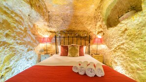 A bed in a cave-like room with a red bedspread, pillows, and rolled towels. - Casa De La Fredeswinda: Charming Andalusian Rural Getaway (Peñaflor)