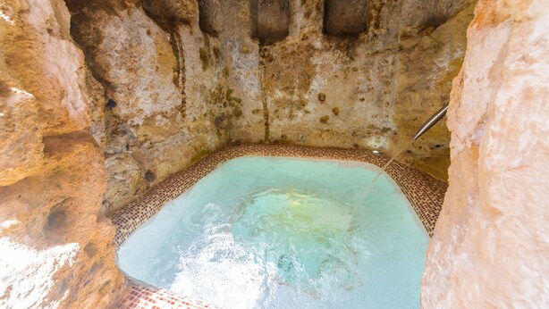 A hot spring with a tiled floor, a metal faucet, and a stone wall with three small openings. - Casa De La Fredeswinda: Charming Andalusian Rural Getaway (Peñaflor)