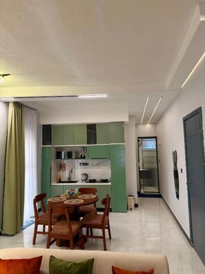 Ein modernes Wohnzimmer mit Essbereich, Küchenschränken in Grün und einer Tür zu einem anderen Raum.