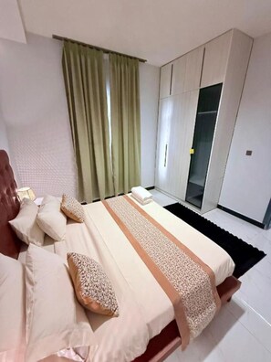 Ein Schlafzimmer mit einem Bett, Kissen, einem Nachttisch, einem Fenster mit Vorhängen und einem Kleiderschrank.