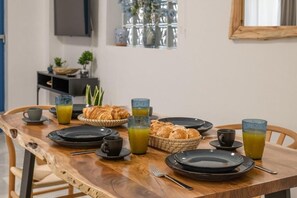 Ein Frühstückstisch ist gedeckt mit Tellern, Tassen und Croissants, im Hintergrund sind ein Fernseher und Pflanzen zu sehen.