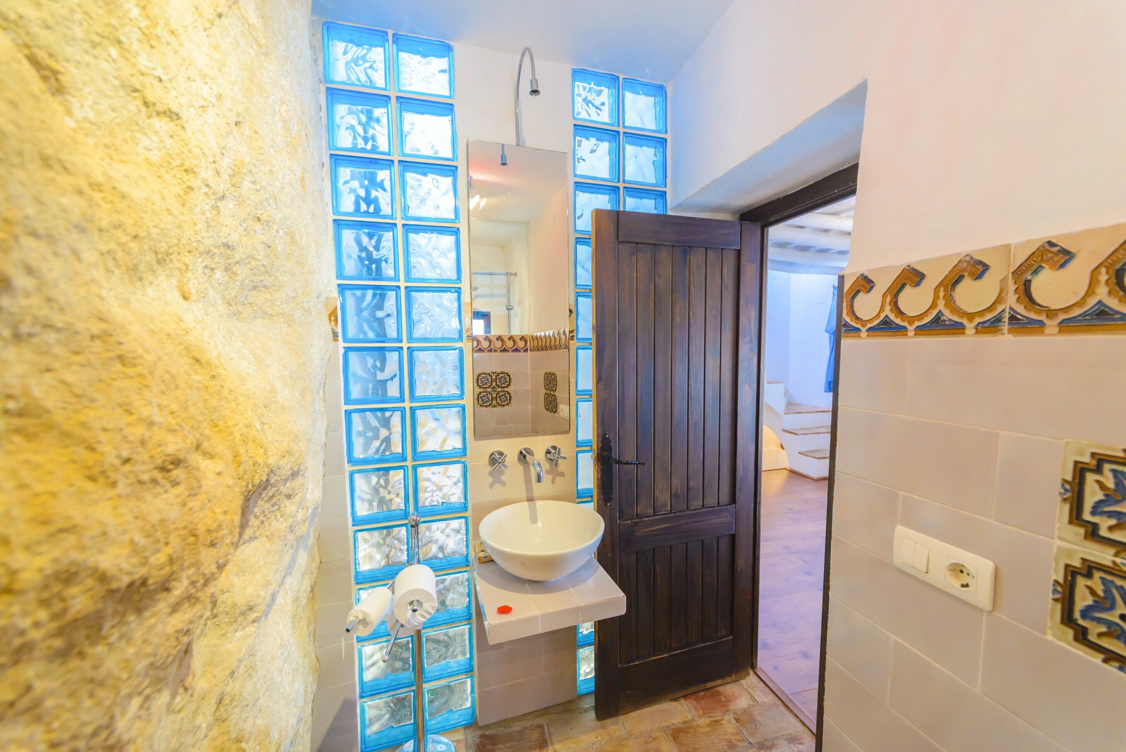 A bathroom with a stone wall, a white sink, a mirror, and a shower.
