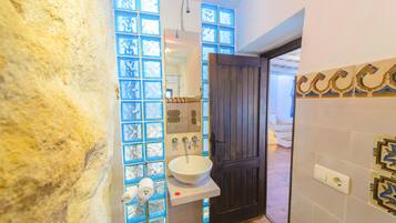 A bathroom with a stone wall, a white sink, a mirror, and a shower.