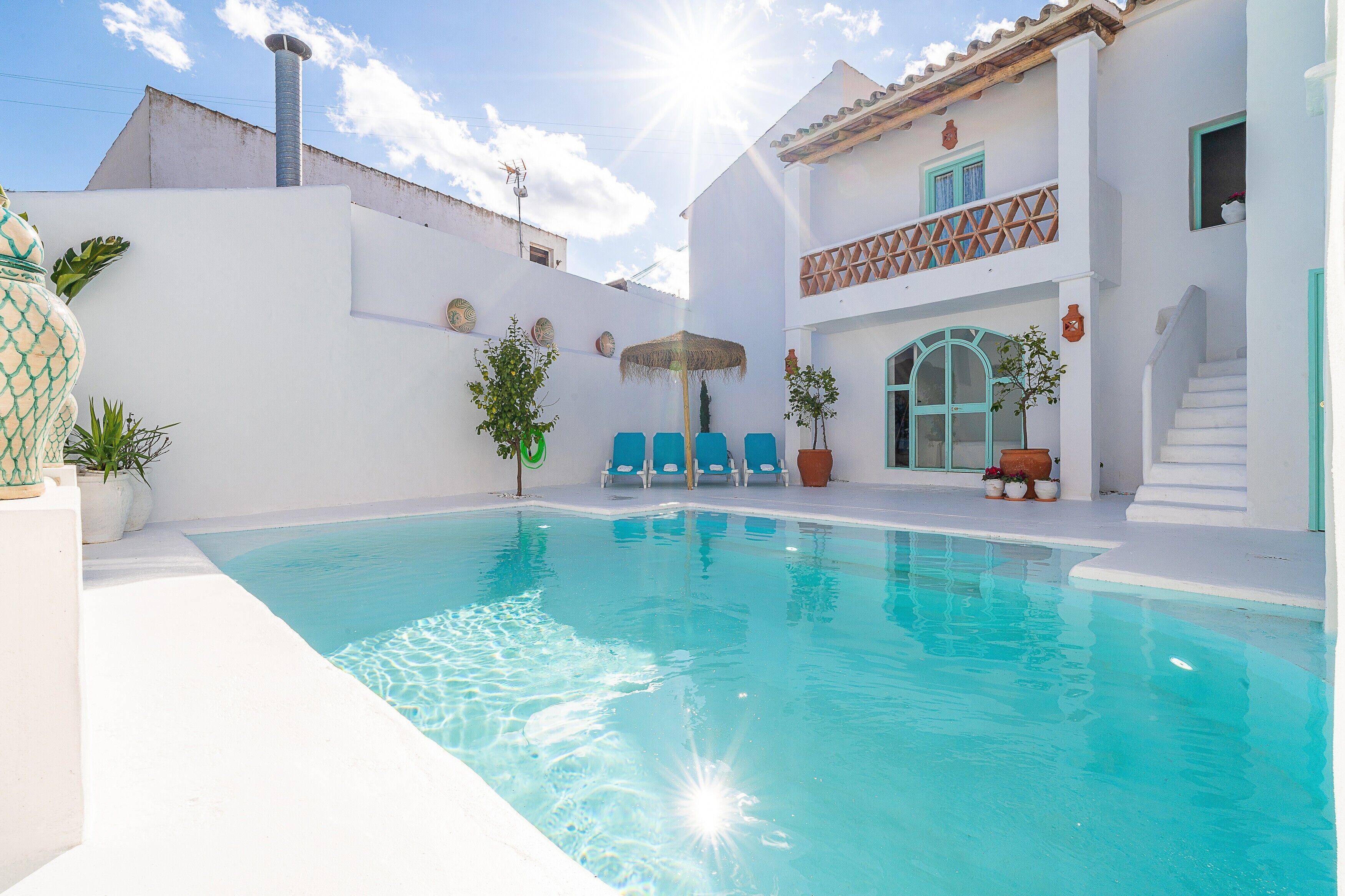 Ein Swimmingpool mit weißer Außenwand, blauen Stühlen und einer Treppe, die zu einem Balkon führt.