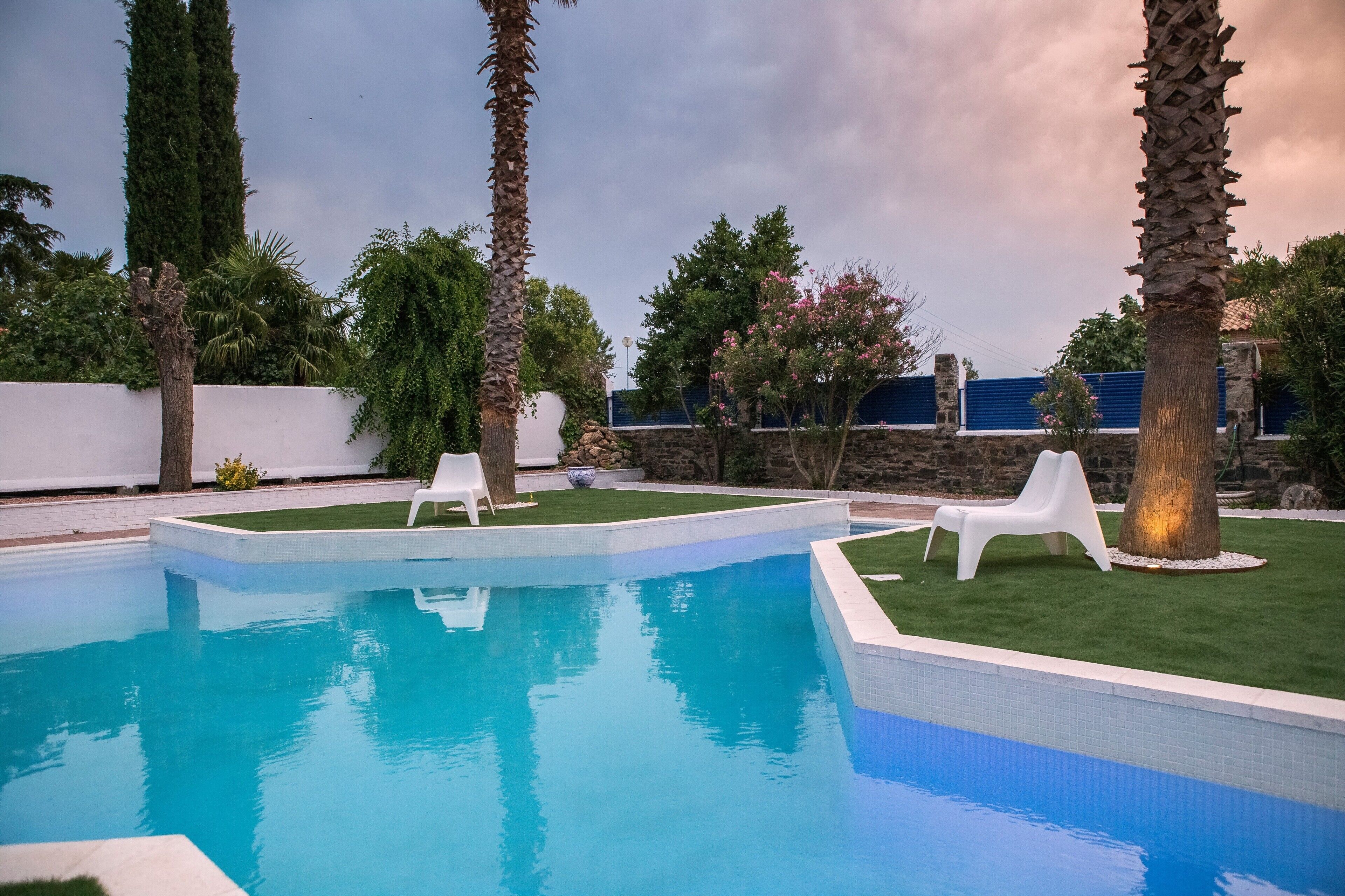 A swimming pool with white lounge chairs and palm trees.