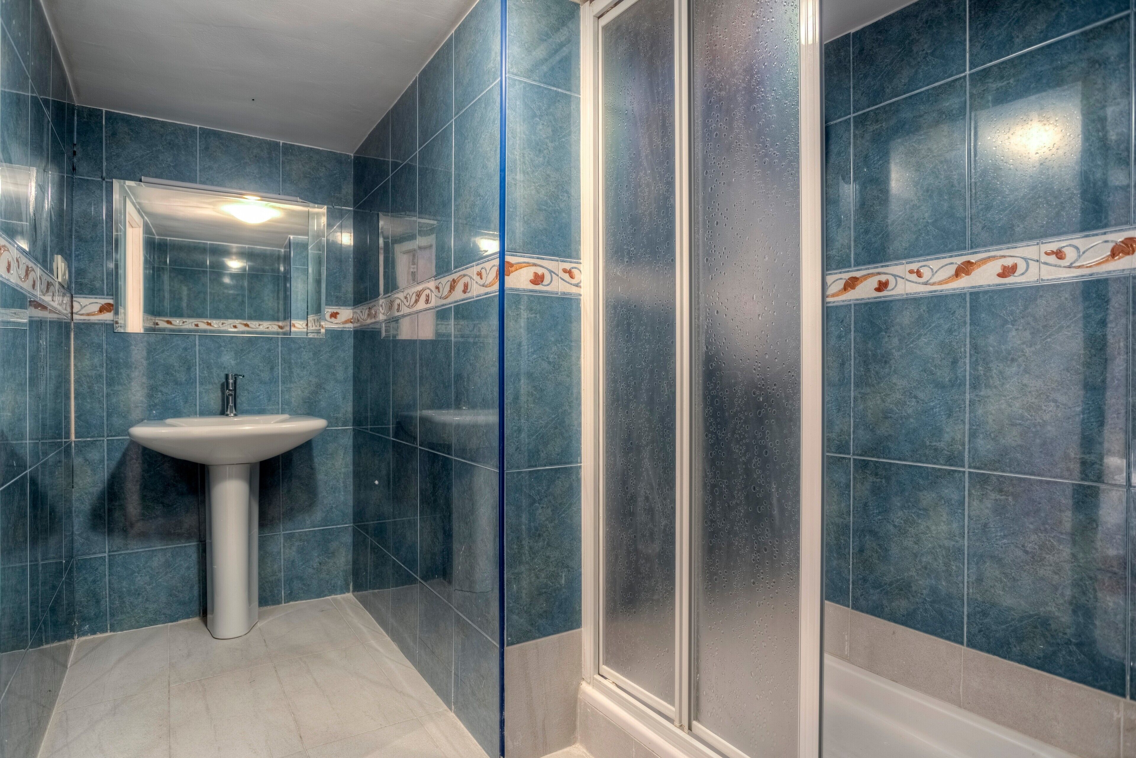 A bathroom with blue tiles, a white sink, and a glass shower enclosure.