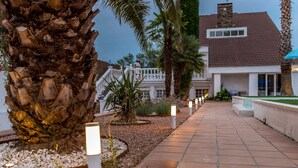 A pathway leading to a house with a white fence, palm trees, and a stone wall.