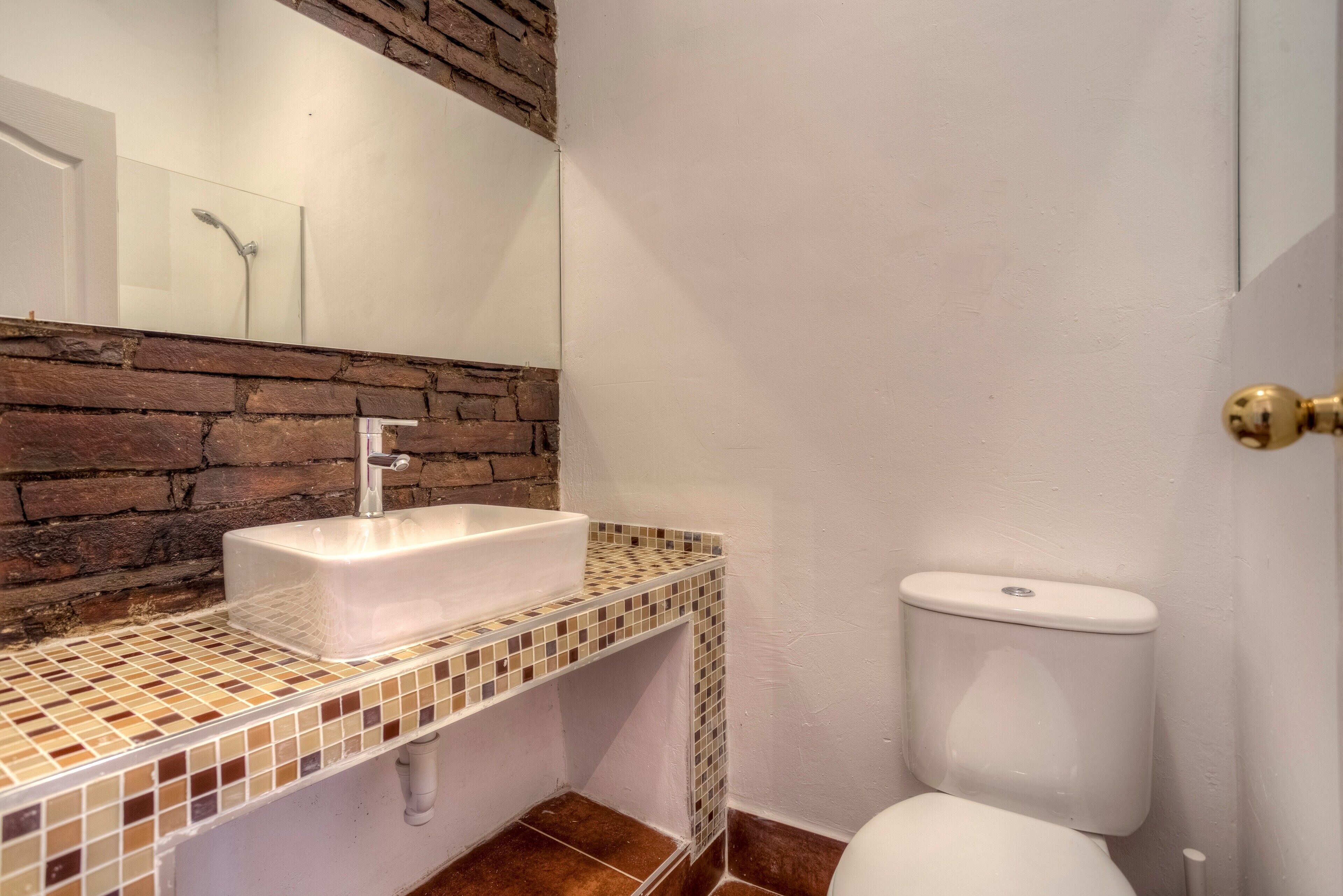 Une salle de bain avec un lavabo blanc, un mur recouvert de carreaux, des toilettes et un miroir.