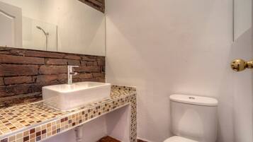 Une salle de bain avec un lavabo blanc, un mur recouvert de carreaux, des toilettes et un miroir.