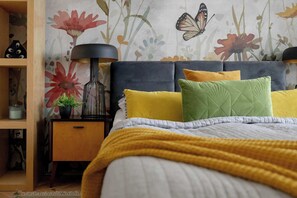 A bedroom with a bed, a nightstand, a lamp, and a floral wallpaper.