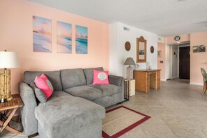 A living room with a grey sofa, a wooden side table, a lamp, and a desk with a mirror. - Summer Deal Beachfront Kona Condo with White Sand Beach Access (Kona)