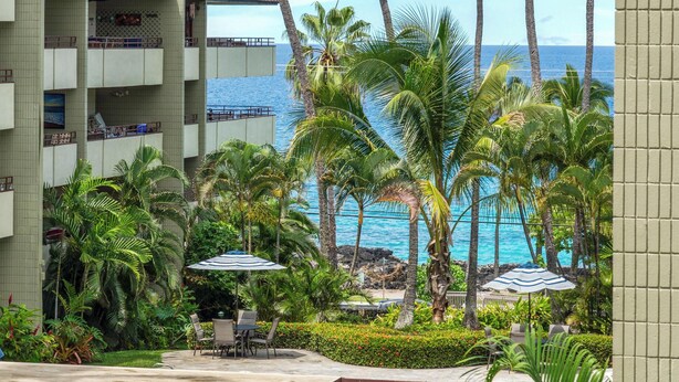 Un espace piscine d’hôtel offrant une vue sur l’océan, des palmiers et un immeuble doté de balcons.