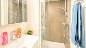 Une salle de bain avec un lavabo blanc, une cabine de douche en verre et une serviette bleue suspendue à un porte-serviettes.