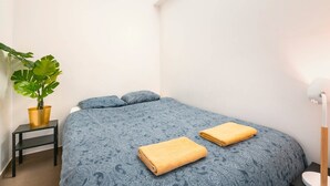 Une chambre à coucher avec un lit, deux oreillers, une table de chevet avec une plante et une lampe.