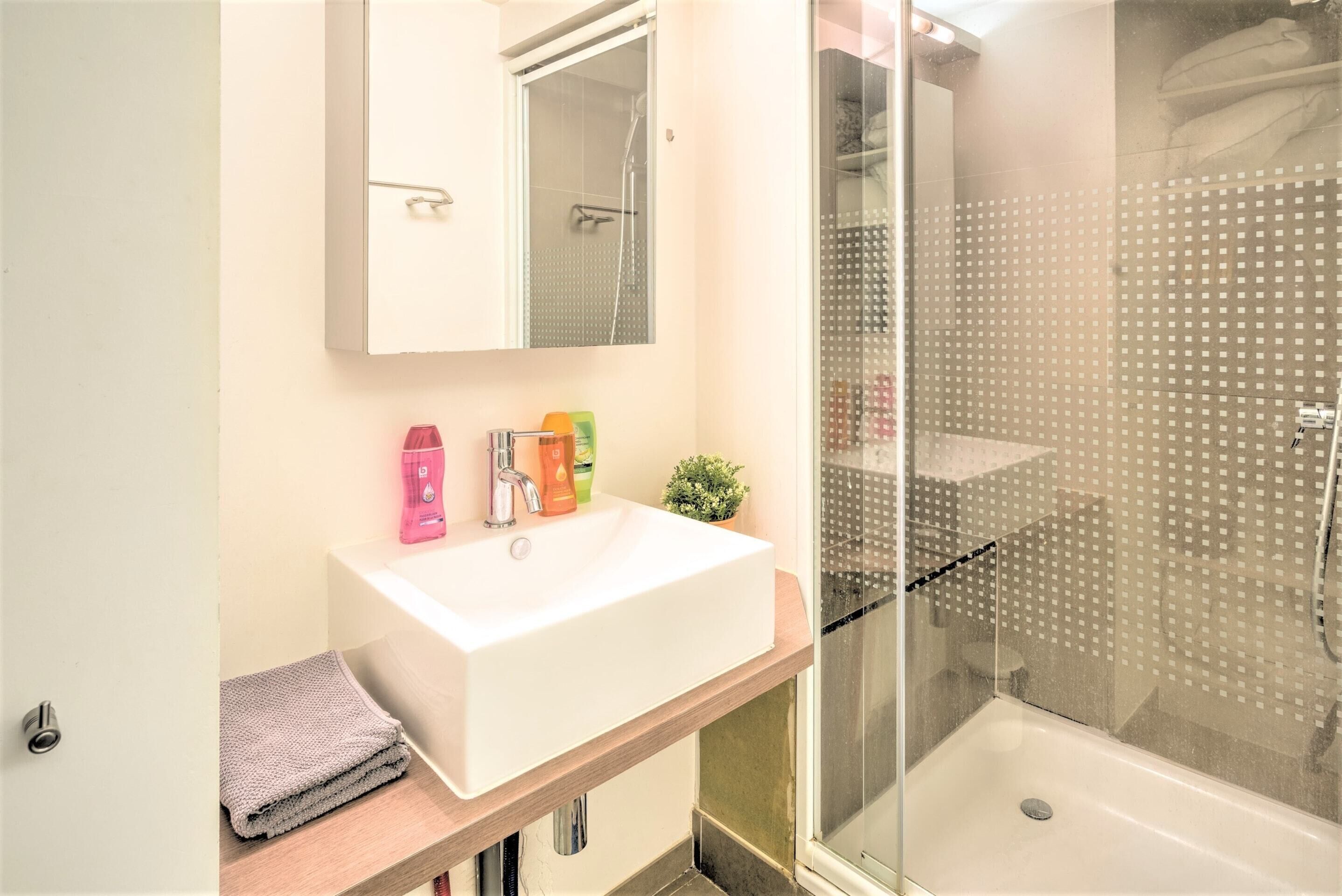 Un baño con lavamanos blanco, espejo y cabina de ducha.