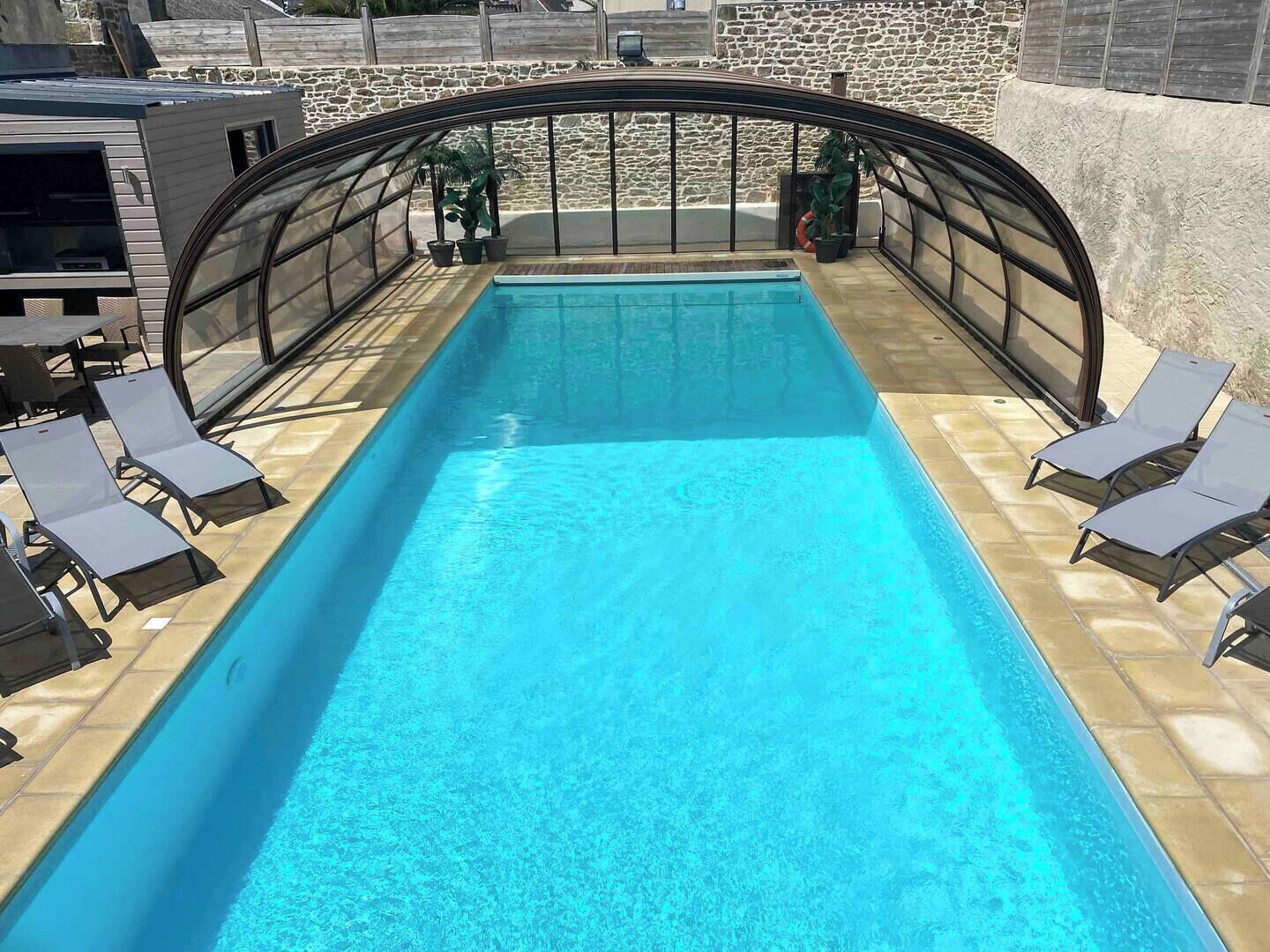 A rectangular pool with clear blue water, surrounded by a glass enclosure, and equipped with sun loungers.