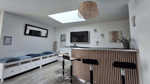 A modern living room with a sofa, a TV, a bar area, and a ceiling light fixture. - Villa des Halles - 14 to 15 pers - Private swimming pool (Plouescat)