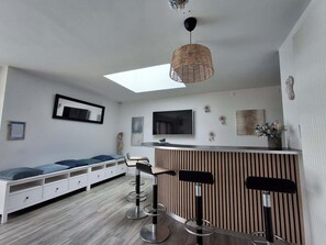 A modern living room with a sofa, a TV, a bar area, and a ceiling light fixture. - Villa des Halles - 14 to 15 pers - Private swimming pool (Plouescat)
