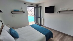 A bedroom with a bed, a TV, a window, and a door leading to a pool. - Villa des Halles - 14 to 15 pers - Private swimming pool (Plouescat)
