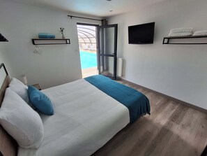 A bedroom with a bed, a TV, a window, and a door leading to a pool. - Villa des Halles - 14 to 15 pers - Private swimming pool (Plouescat)