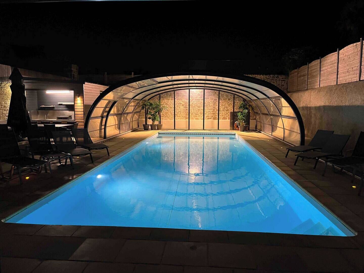 Una piscina con techo curvo, rodeada de sillas de descanso y plantas en macetas.