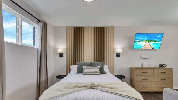 A bedroom with a bed, a TV, a wooden dresser, and a window with curtains. - New Columbus Studio Steps from Downtown (Columbus)