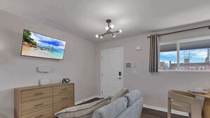 Una sala moderna con una televisión de pantalla plana, un mueble de madera, un sofá gris, una mesa de comedor con una silla y una ventana con cortinas.