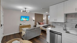 Ein modernes Hotelzimmer mit einer Küchenzeile, einem Bett mit Blick, einem grauen Sofa und einem Flachbildfernseher.