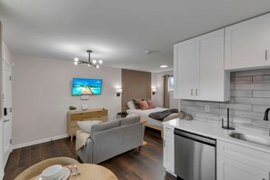 Una habitación de hotel moderna con kitchenette, cama con vistas, sofá gris y televisor de pantalla plana.