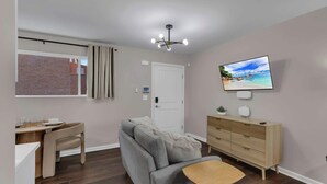 Ein modernes Wohnzimmer mit einem grauen Sofa, einem Holzesstisch, einem an der Wand befestigten Fernseher und einer Deckenleuchte.