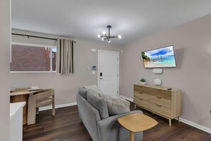 Una sala de estar moderna con un sofá gris, una mesa de comedor de madera, un televisor montado en la pared y una lámpara en el techo.