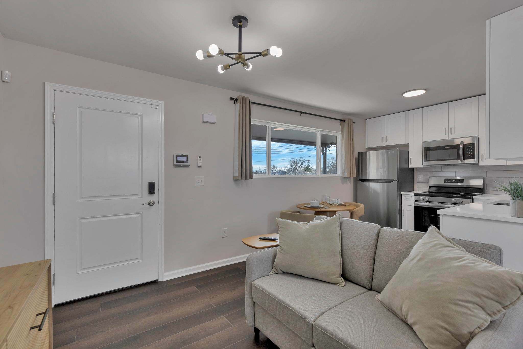 A modern kitchen with stainless steel appliances, a grey sofa with cushions, and a ceiling light fixture.