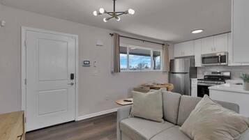 A modern kitchen with stainless steel appliances, a grey sofa with cushions, and a ceiling light fixture.