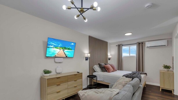 Ein modernes Schlafzimmer mit Bett, Sofa, Fernseher und Kommode.