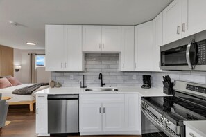 Una cocina moderna con armarios blancos, lavavajillas de acero inoxidable, microondas negro y horno empotrado.