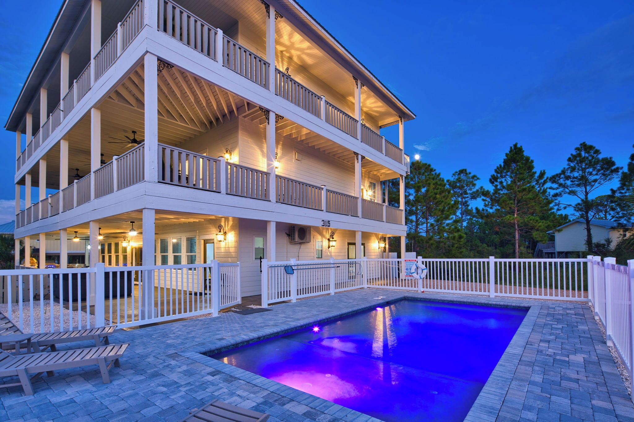 A multi-story building with a pool, outdoor lighting, and a white fence.