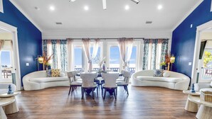 Ein geräumiges Wohnzimmer mit einer gebogenen weißen Couch, einem Esstisch mit Stühlen und Blick durch große, mit Vorhängen drapierten Fenster.