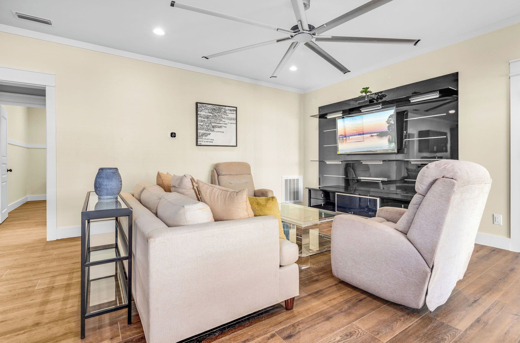 Un salon comprenant un canapé, un fauteuil, une table basse en verre et un ventilateur de plafond.
