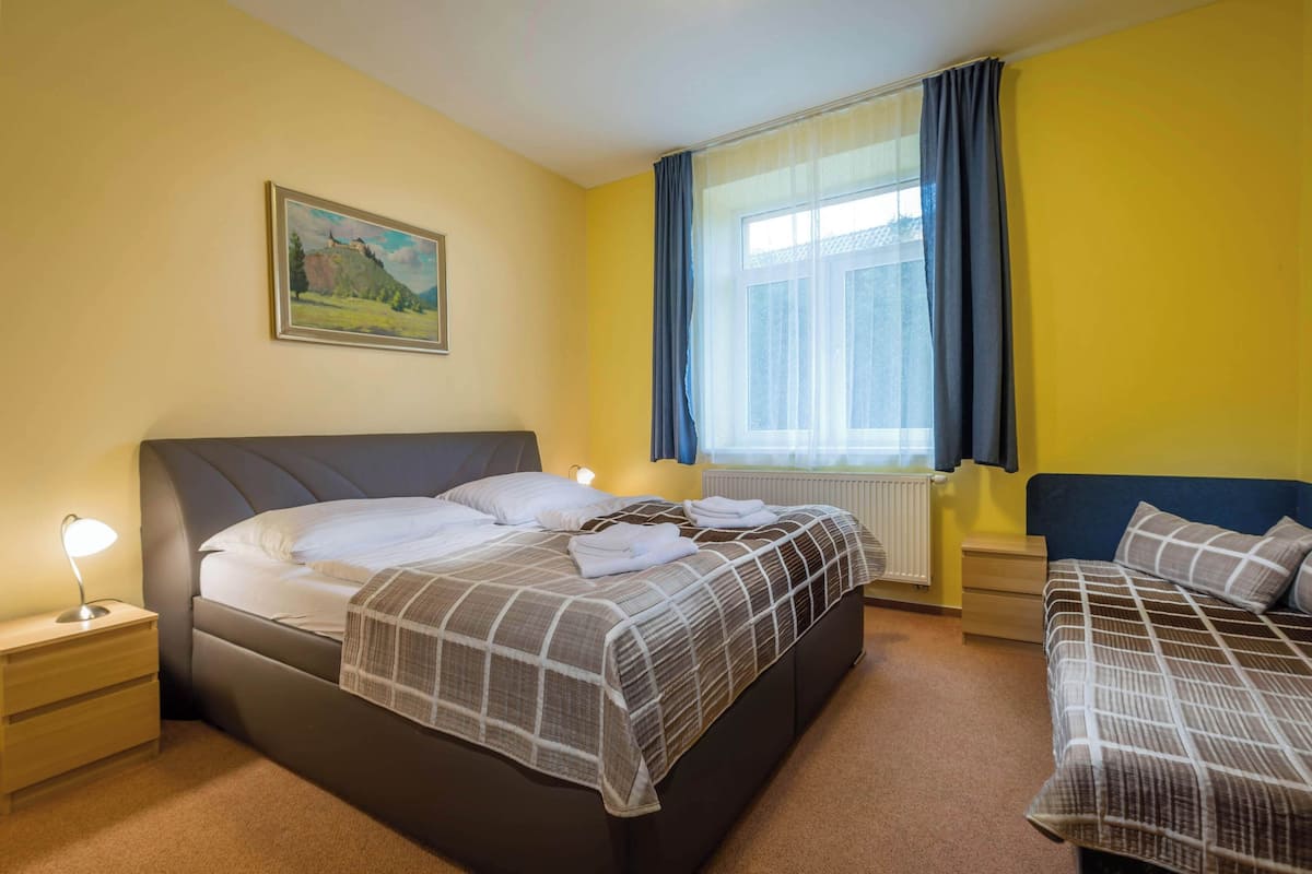 Un dormitorio con una cama, una mesita de noche, una lámpara, una ventana con cortinas y un cuadro en la pared.
