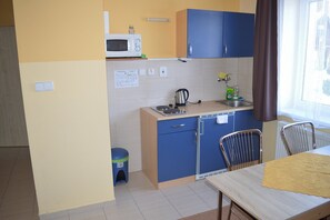 Una cocina compacta con microondas, hervidor, lavabo y una mesa de comedor con sillas.