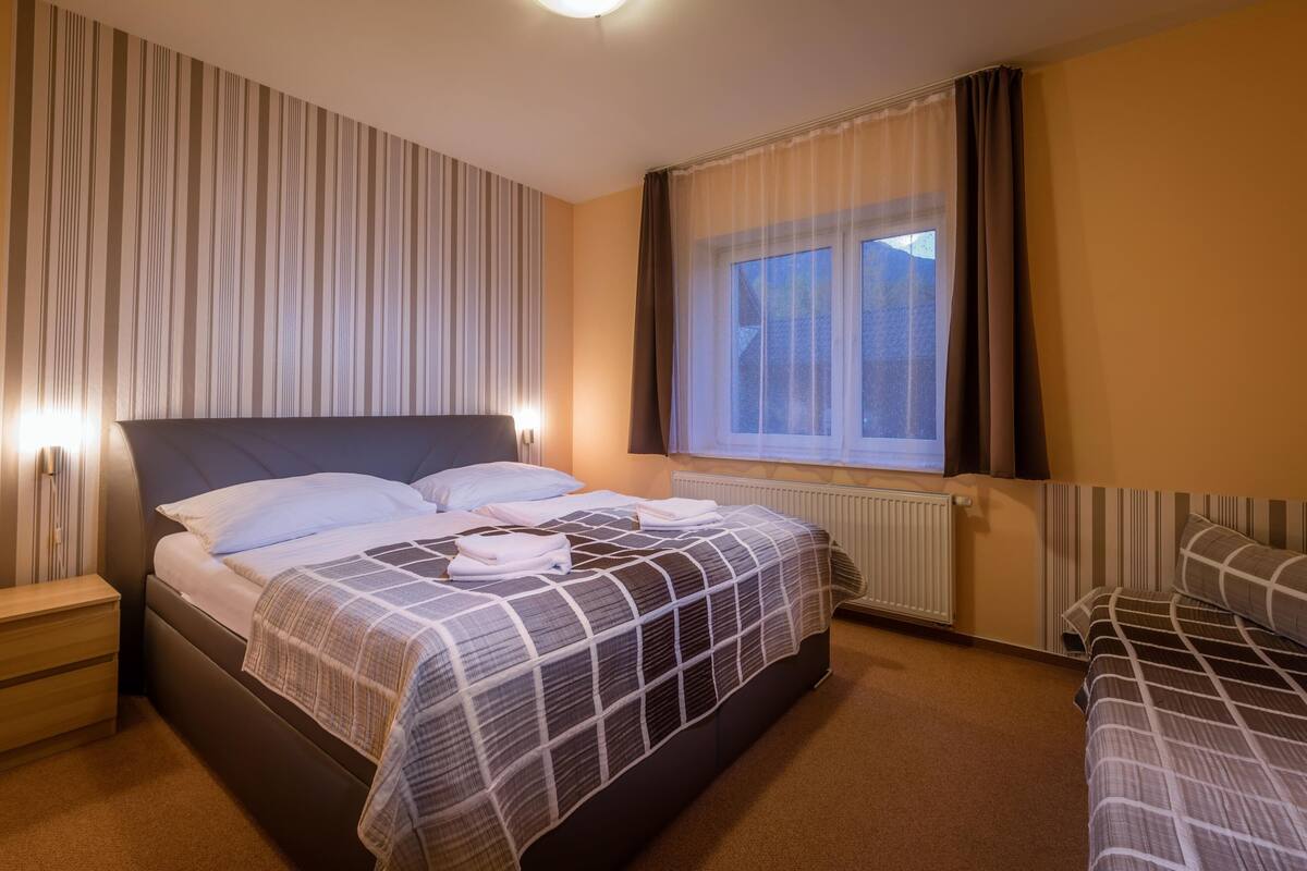 Una habitación de hotel con una cama grande, mesitas de noche, una ventana con cortinas y un radiador.