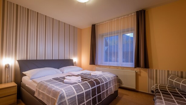 A hotel room with a large bed, bedside tables, a window with curtains, and a radiator. - Miramonti Apartmany (Vysoké Tatry)